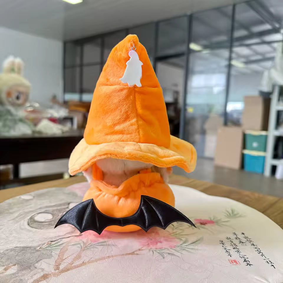 Small plush toy with an orange hat and black bat wings on a floral cushion.
