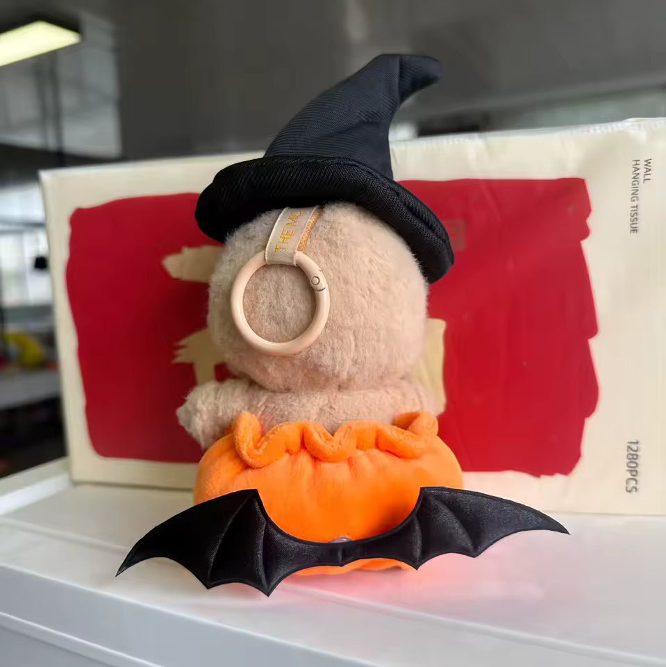 Plush toy dressed as a pumpkin with a witch hat on a white surface