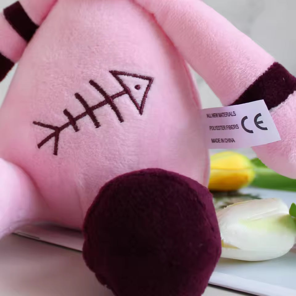 Close-up of a pink plush toy with a fishbone design and a label on a blurred background.